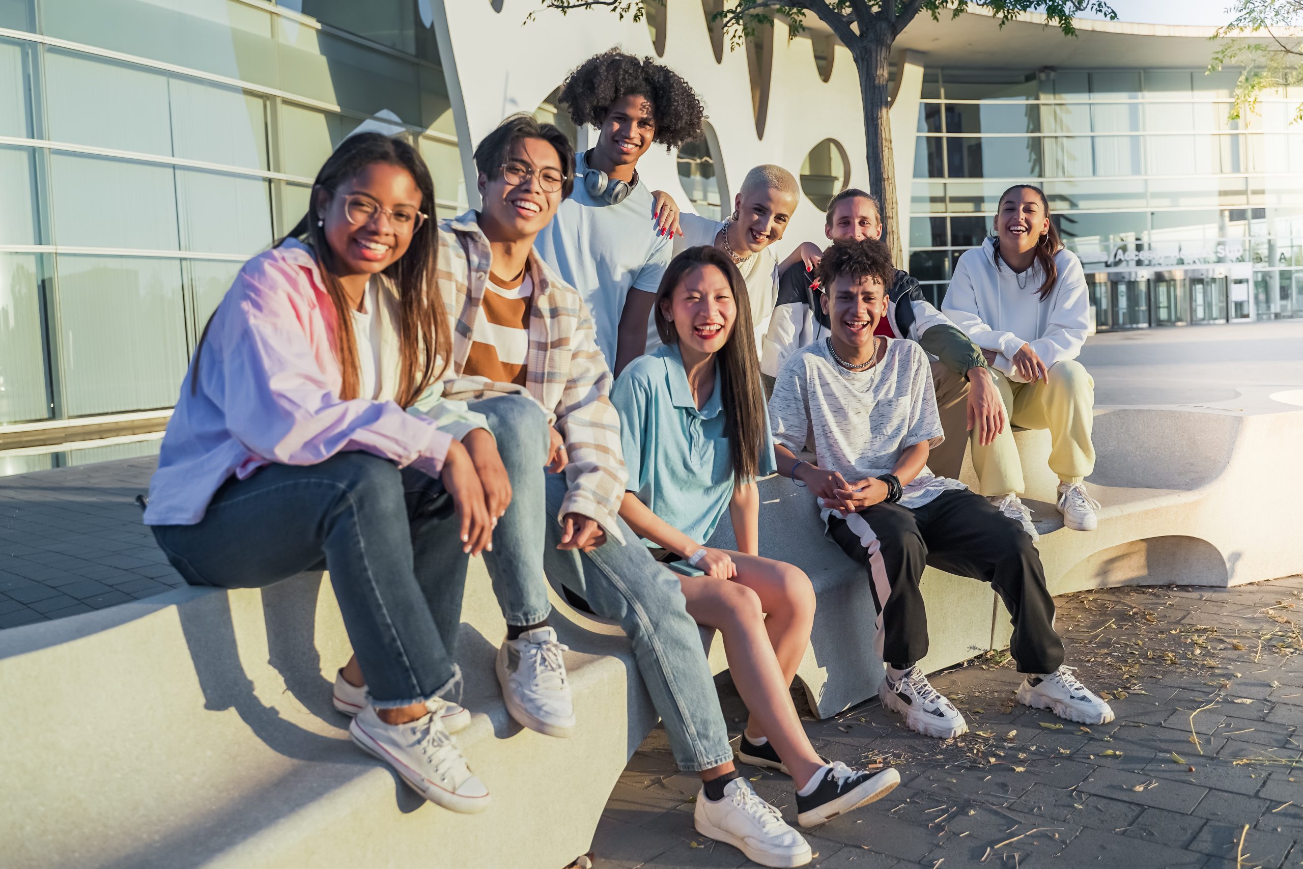 Big group of happy teenage friends looking to the camera in a bench in the street